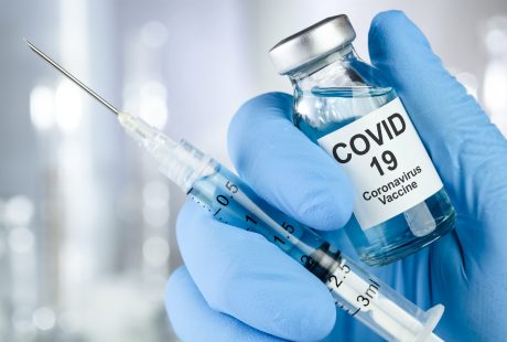 Ręka w rękawicy medycznej trzyma fiolkę ze szczepionką na COVID-19 i strzykawkę z igłą