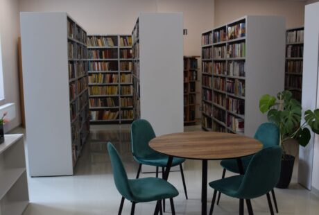 Nowoczesne wnętrze biblioteki z półkami na książki, okrągłym drewnianym stołem i trzema turkusowymi krzesłami.