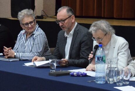 Trzy dojrzałe osoby siedzące przy stole podczas dyskusji panelowej; jeden mężczyzna i dwie kobiety, z mikrofonami i papierami przed sobą.