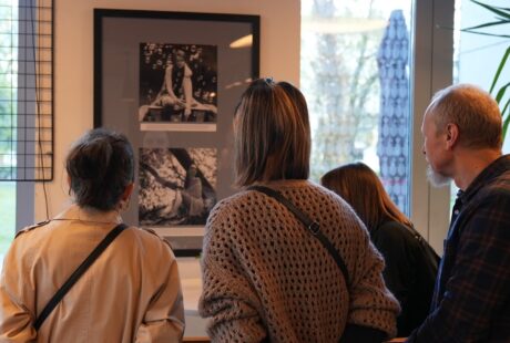 Trzy osoby obserwujące oprawioną w galerię czarno-białą fotografię, z odległym widokiem na dzieła sztuki w tle.