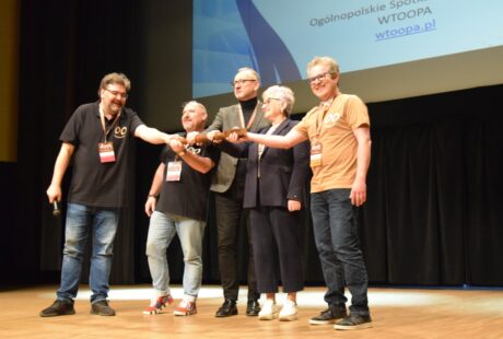 Pięć osób na scenie na konferencji, łączących się za ręce i uśmiechniętych, z wyświetlanym w tle napisem „ogólnopolskie spotkanie wtoopa wtoopa.pl.