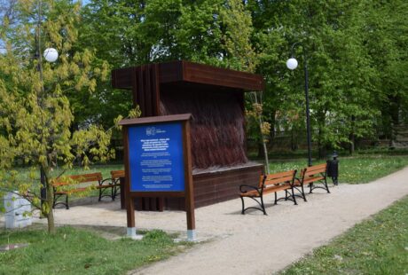Drewniany pawilon z kaskadową fontanną otoczony ławkami parkowymi w bujnym zielonym parku.